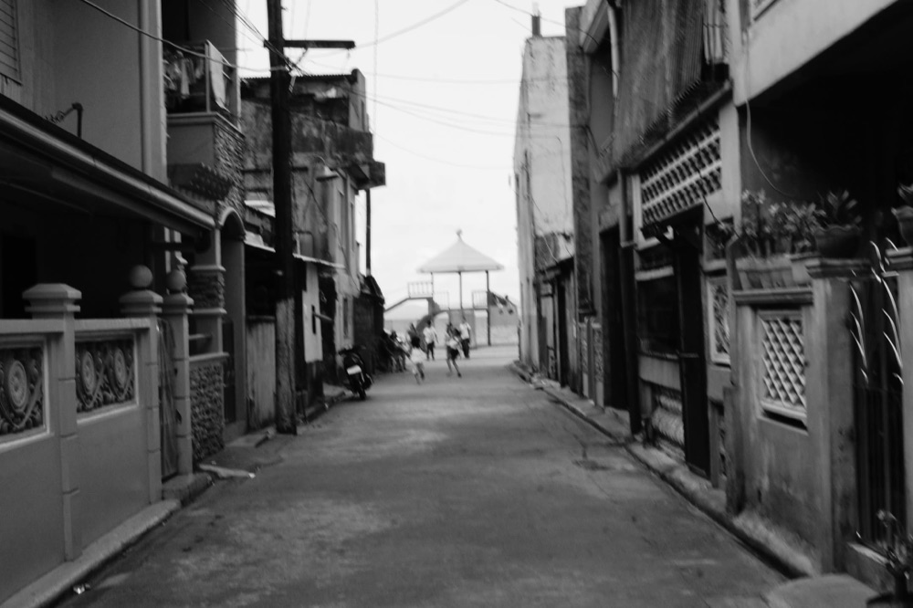 A quiet black and white alley between houses, a gazebo at the far end